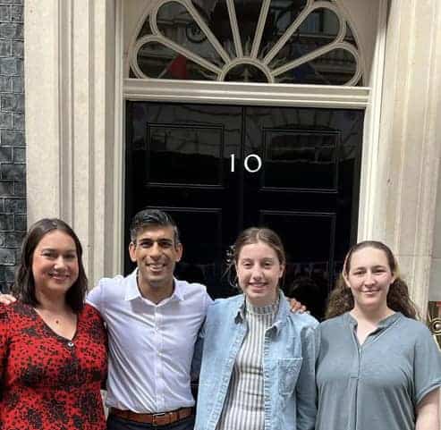The Prime Minister stands with his arms around two young islanders and a YIN youth worker. Behind them is a glossy black door with a white number 10.