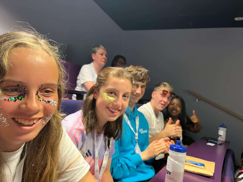 5 young people sitting in a row smiling with glitter make up