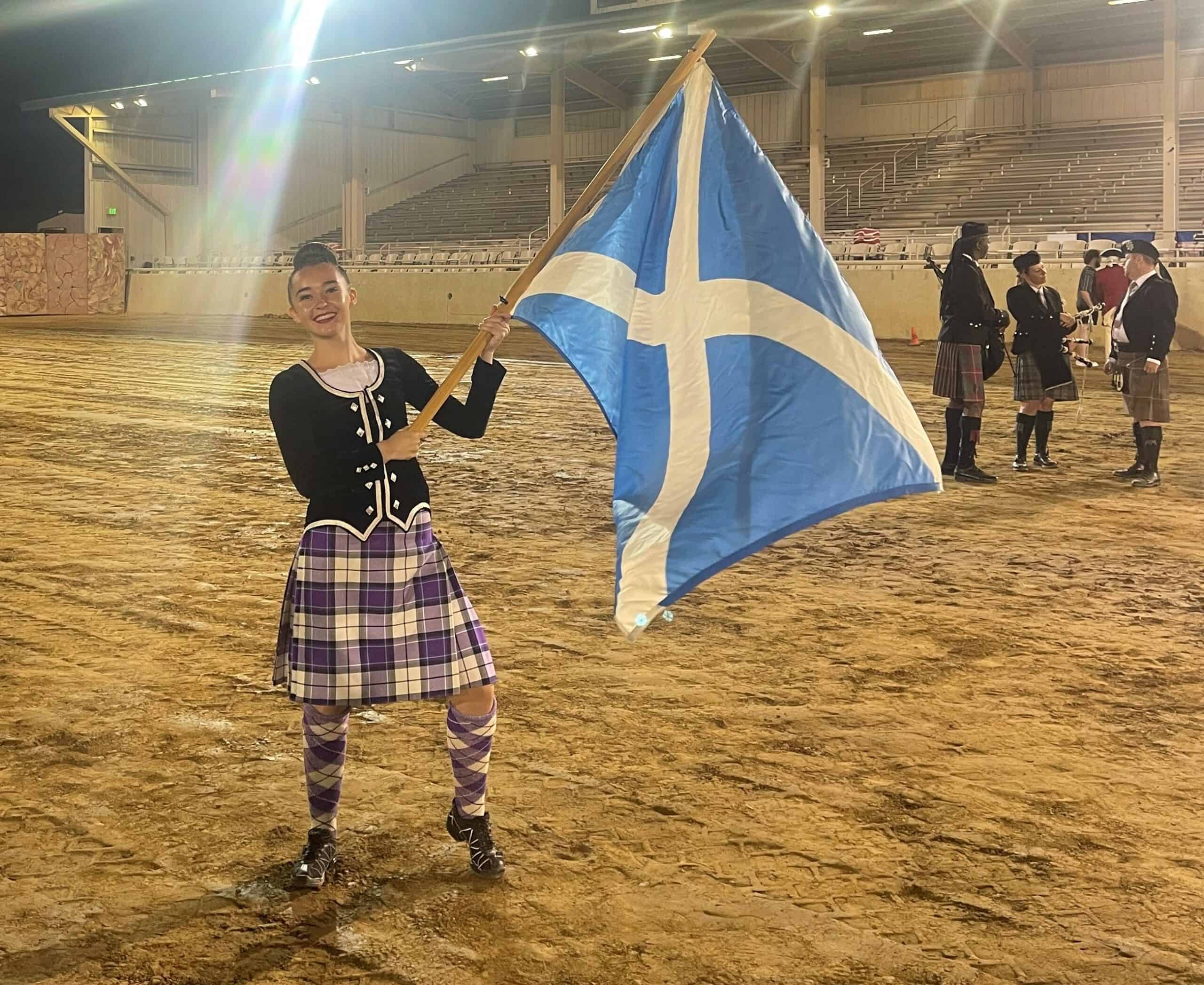 young person in a highland dancing outfit waving a saltire flag