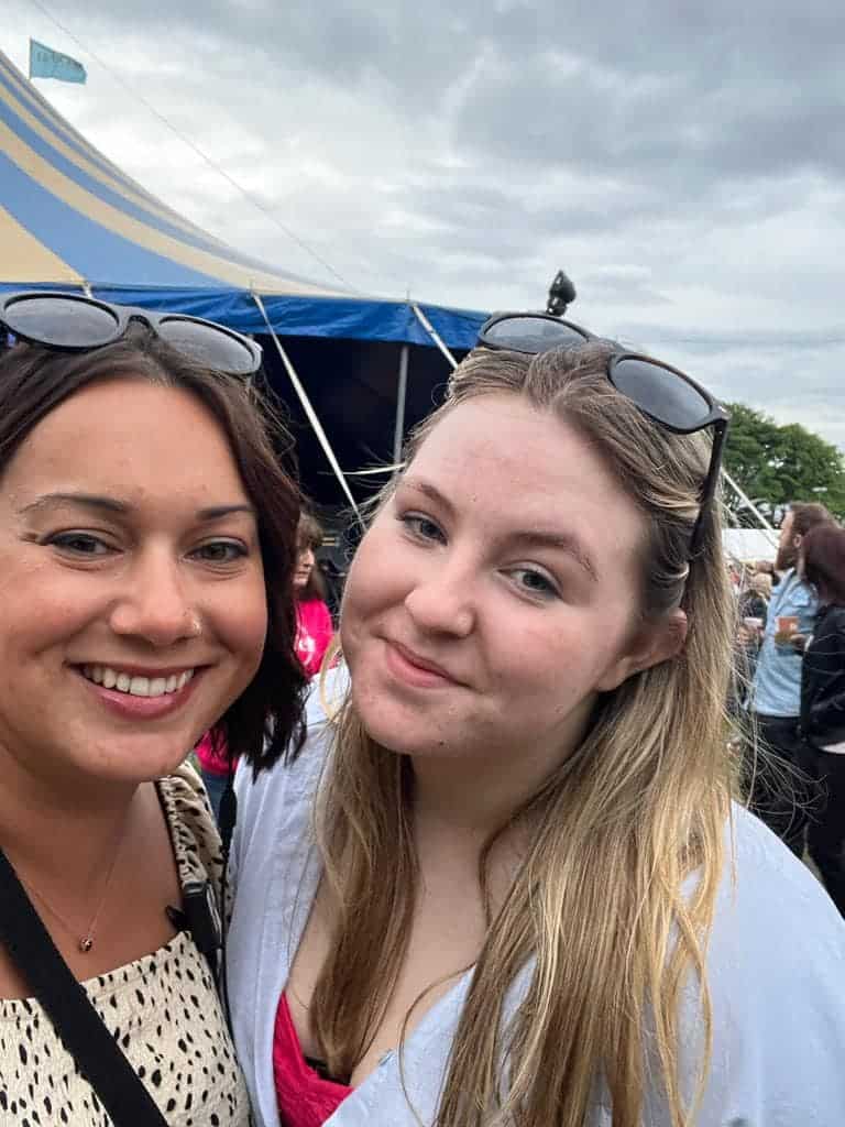 Two people, with glasses on head. smiling for camera infront of blue and yellow tent. people in background