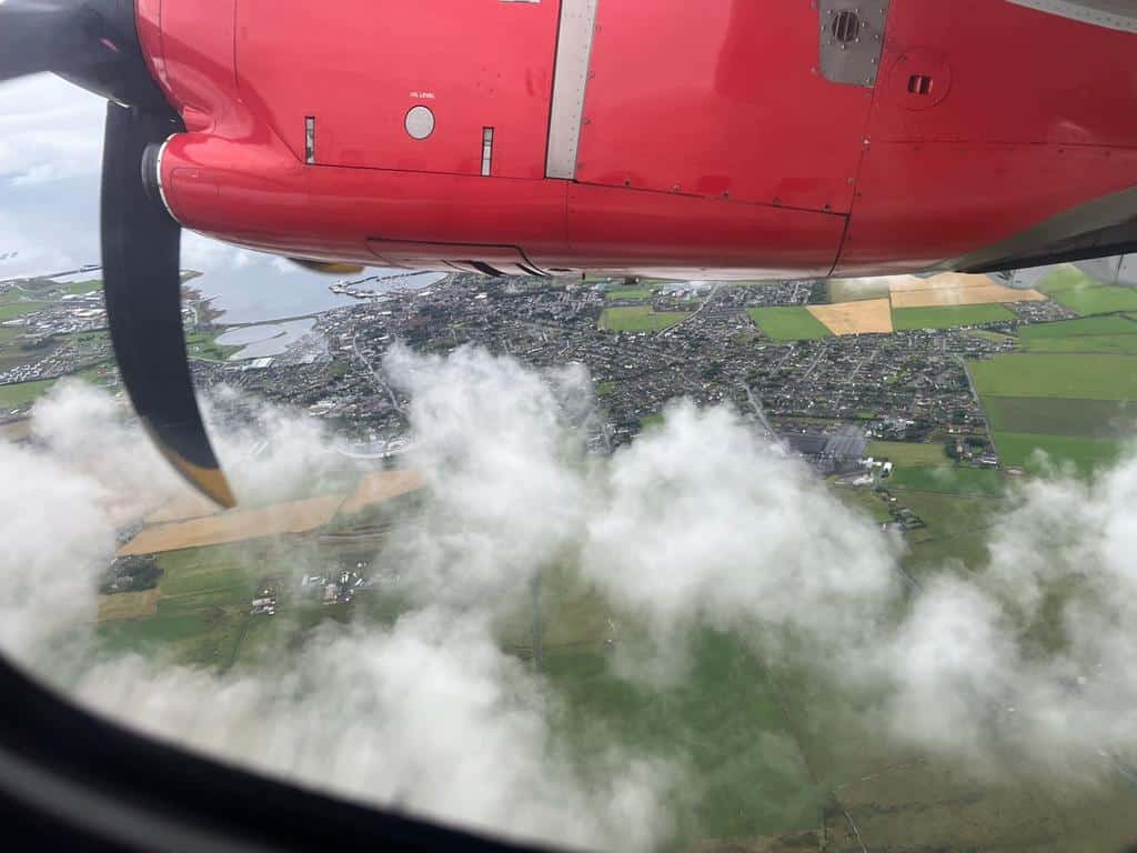 A red propeller plane engine flies through clouds. An island town is visible below.