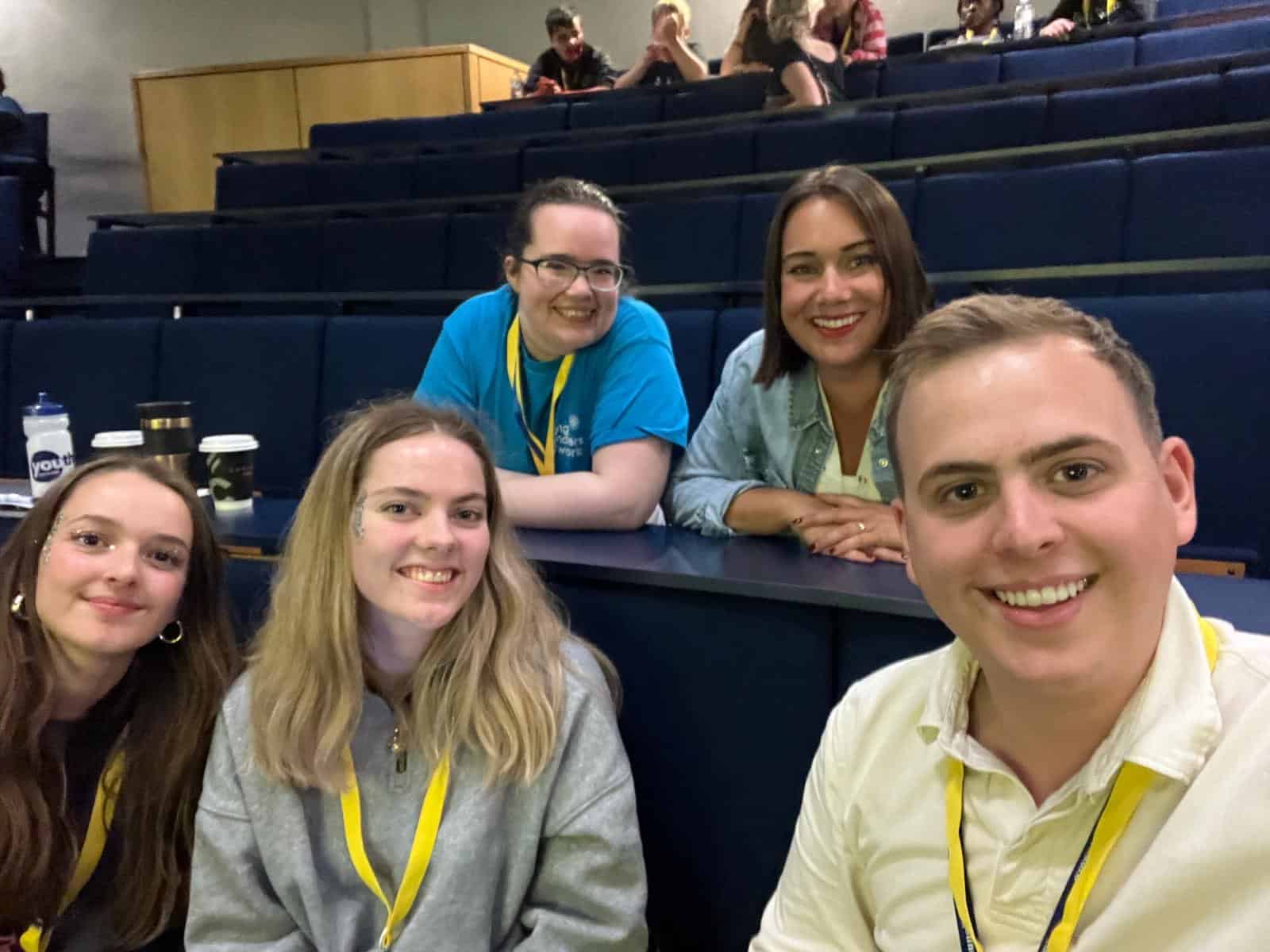 five people sitting in lecture theater smiling at camera