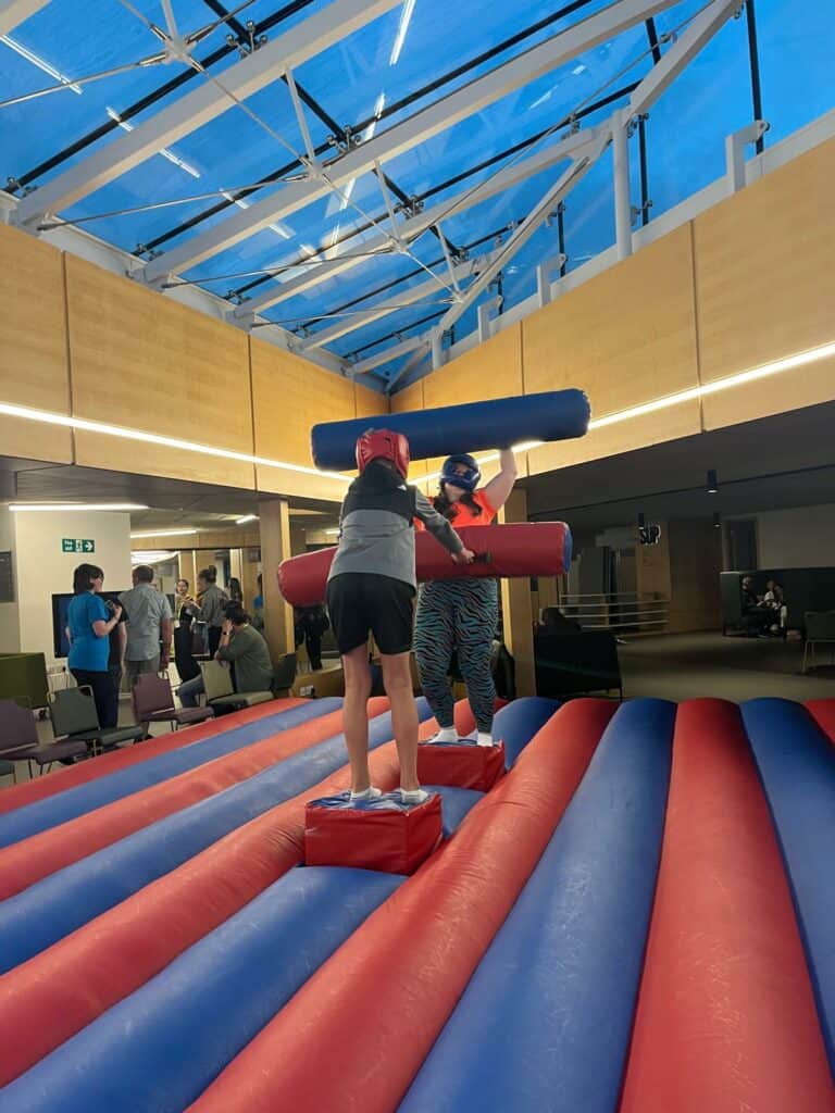 two young people on inflatable challenge trying to knock each other off podiums with inflatable logs