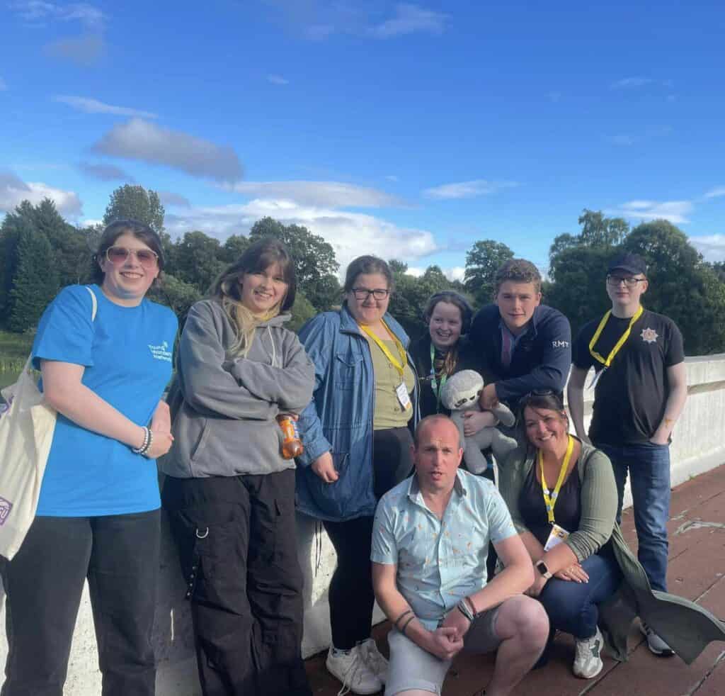 group of young people smiling at camera, standing on a bridge with trees in the background