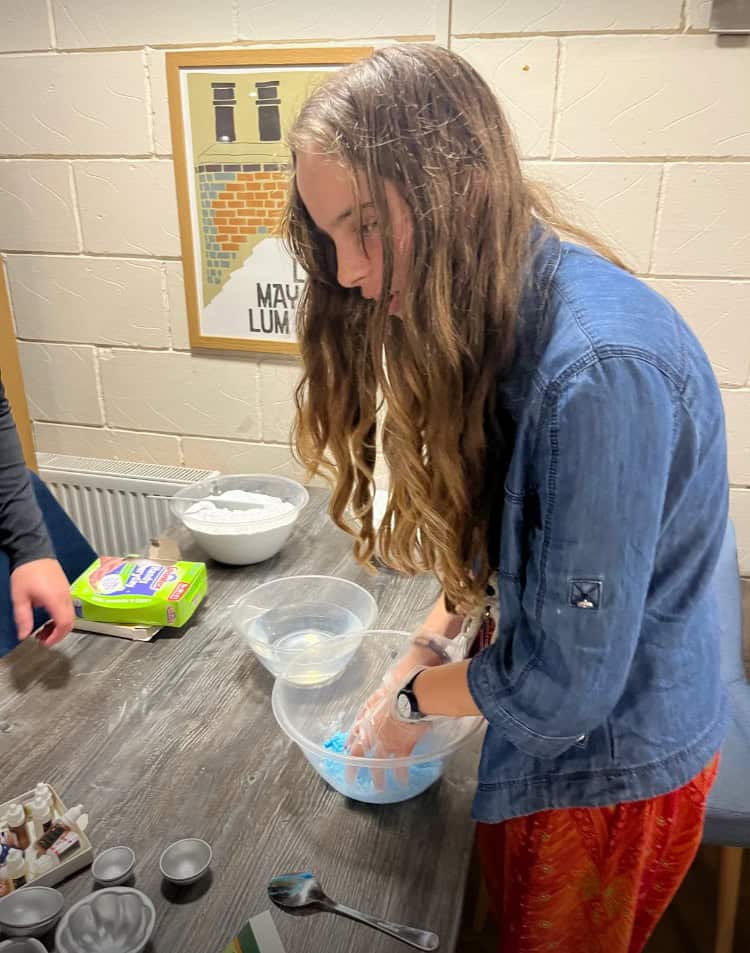 young person with long hair mixing blue powder in a bowl on a table