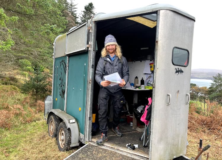 young man standing in a horse box in a wooded area