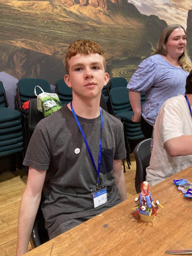 young person smiling and a monster themed cupcake on the table