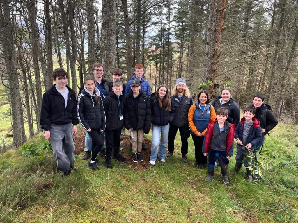 group of young people with three workers standing in a line, smiling a the camera in a woodland