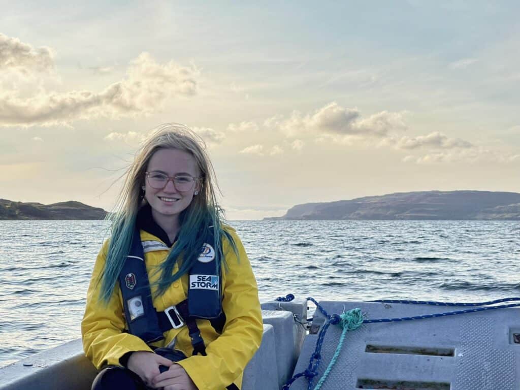 girl in yellow jacket sitting on a boat in the water smiling at the camera