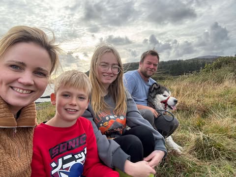 family sitting in grass smiling at camera with a dog on a leash