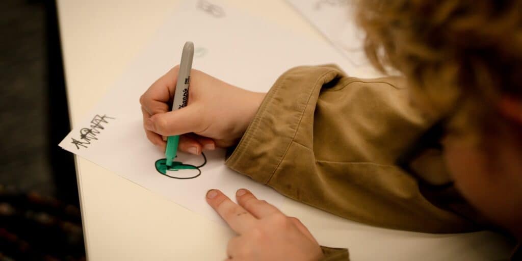 A young person uses a marker pen to outline a story on a sheet of paper.